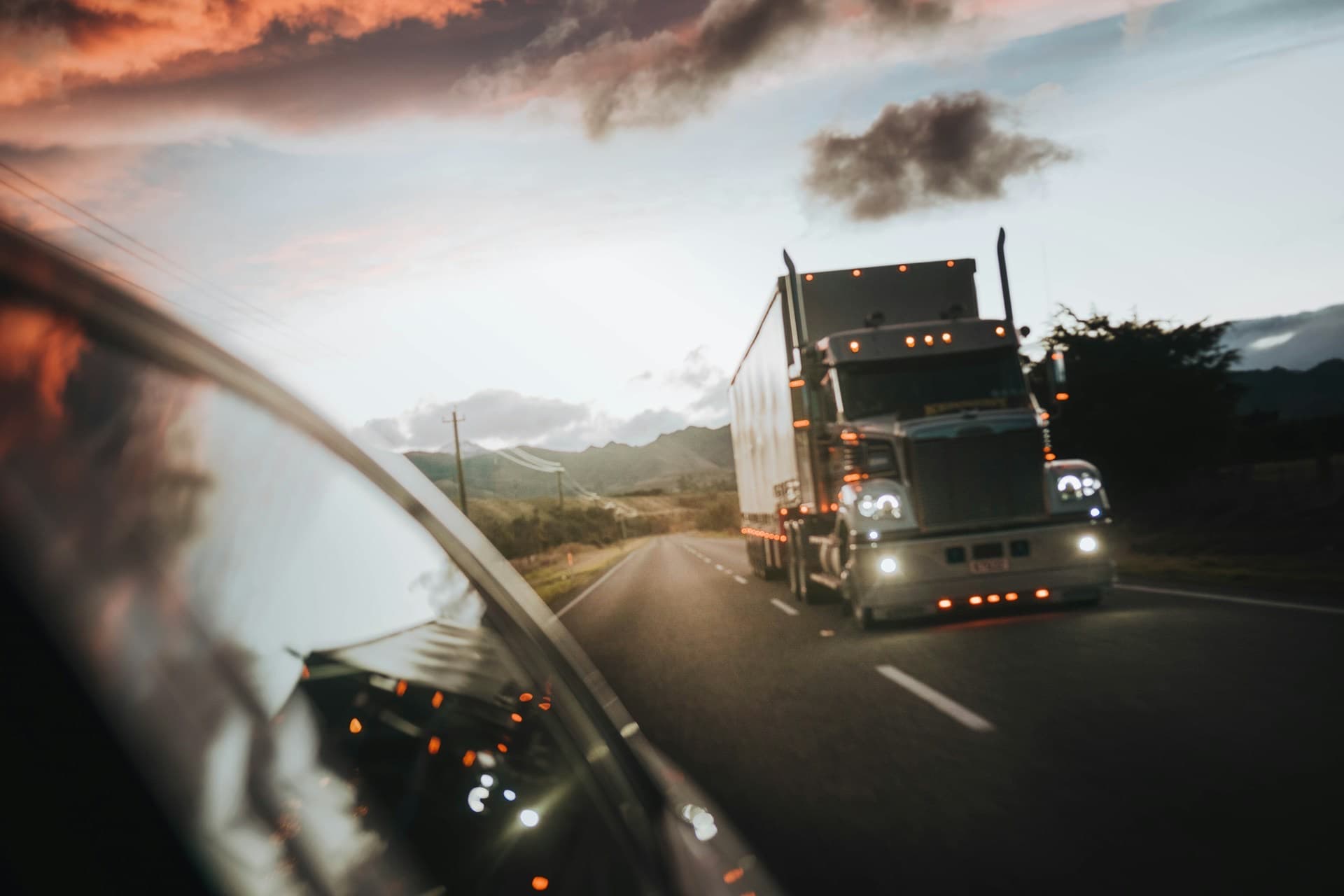 Caminhão com os faróis acesos em uma rodovia ao entardecer
