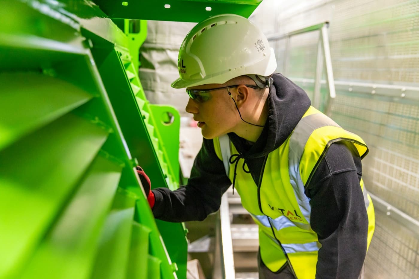 Técnico de capacete e colete inspecionando a montagem de um equipamento
