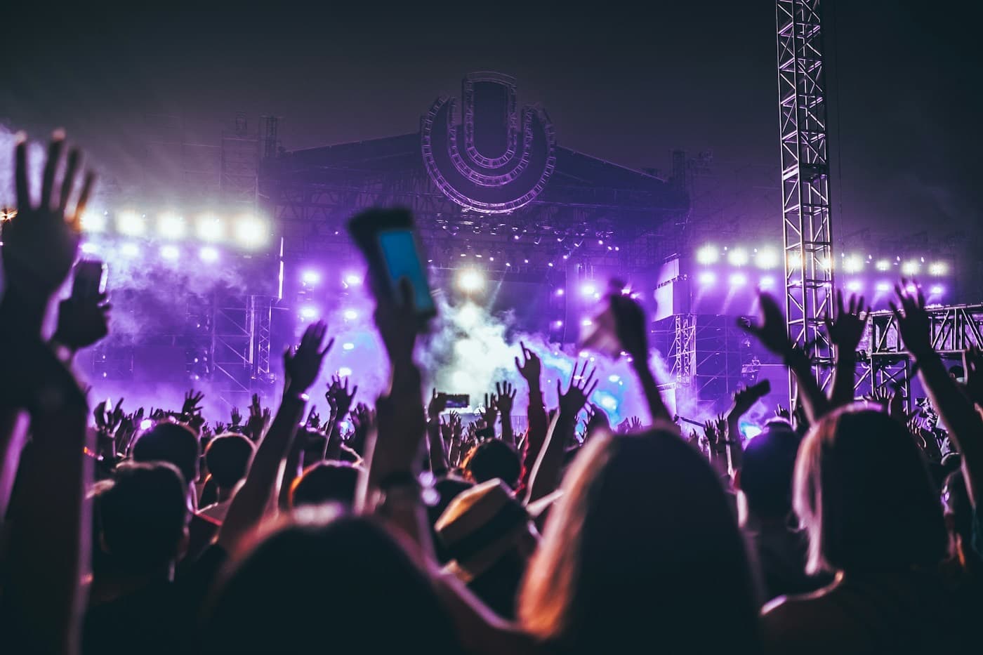 Público de mãos para o alto em frente a um palco iluminado em um festival