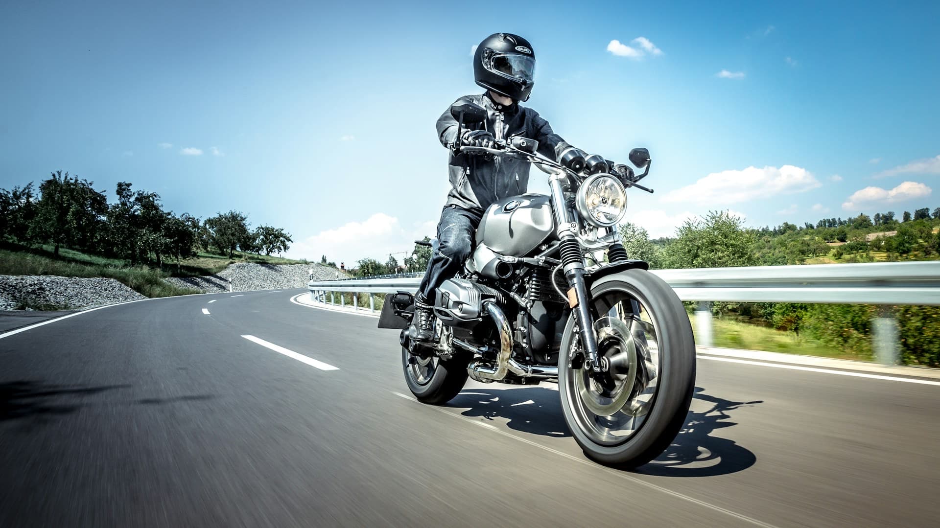 Motociclista equipado pilotando por uma estrada em dia de céu azul