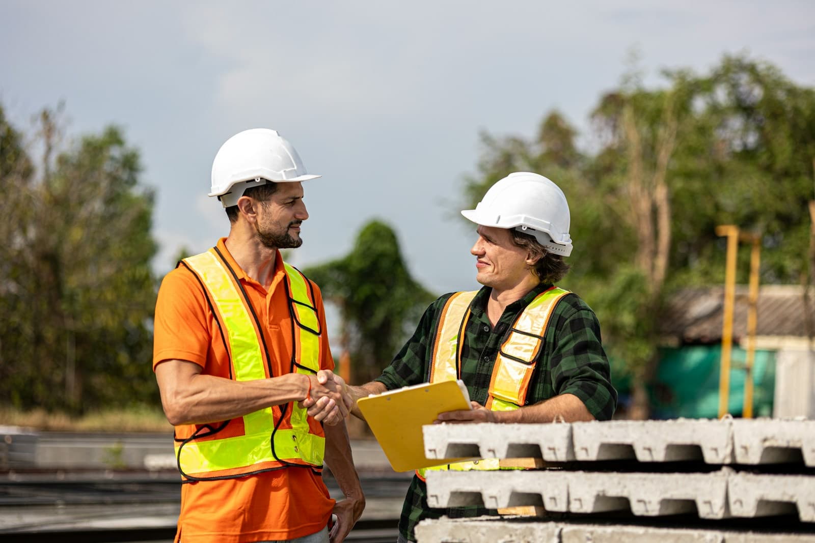 Dois profissionais de capacete apertando as mãos em um canteiro de obras