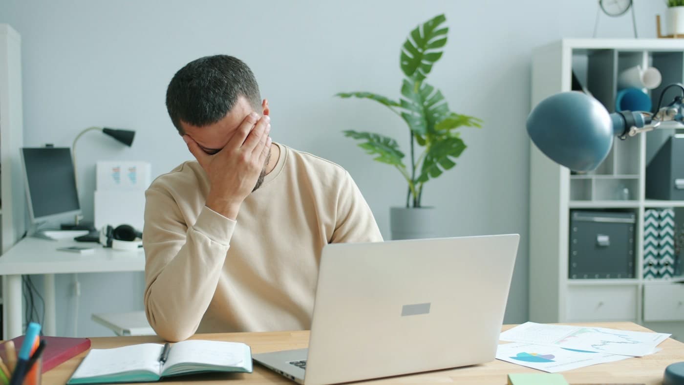 Profissional cansado esfregando o rosto em frente ao notebook