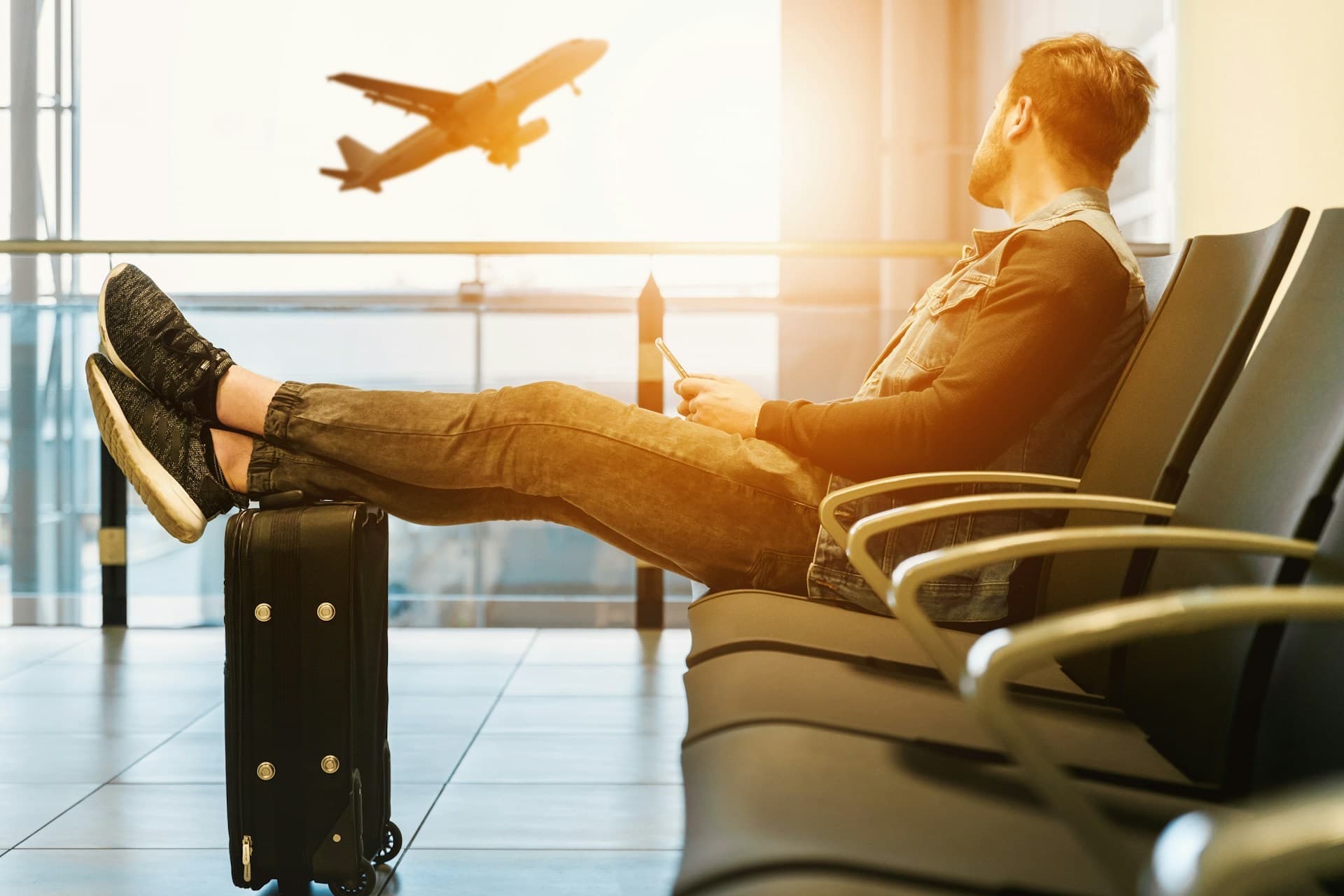 Viajante descansando no aeroporto com os pés sobre a mala enquanto um avião decola