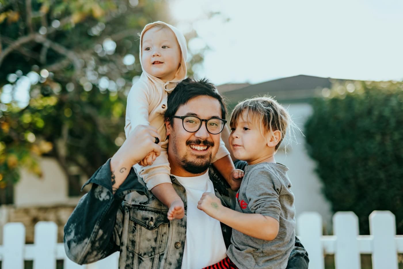 Pai sorrindo com os dois filhos pequenos no colo e nos ombros